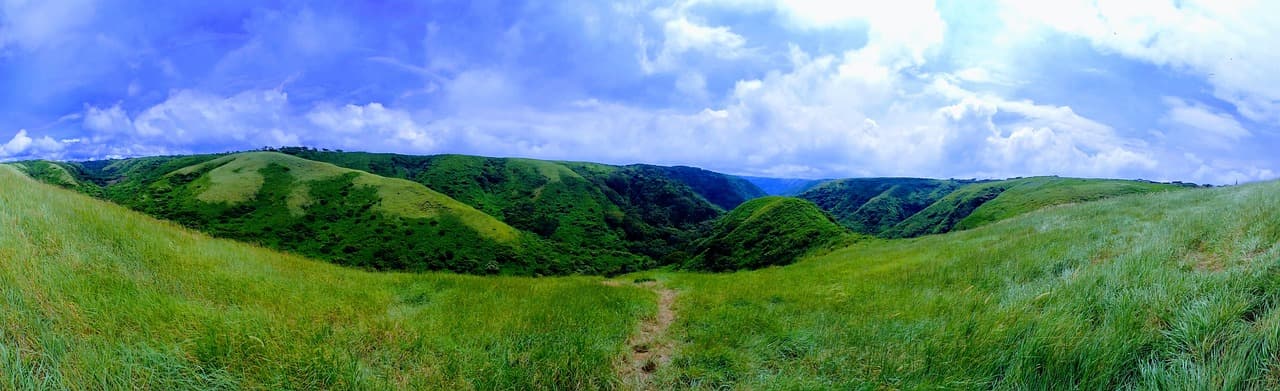 Colina cubierta de hierba verde y campo abierto bajo cielo azul, en el chat de Sébaco