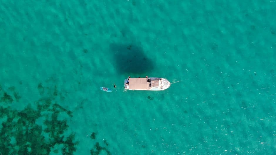 Barca y una persona nadando con tabla en agua turquesa, vistas desde arriba, en el chat de Puerto Morelos