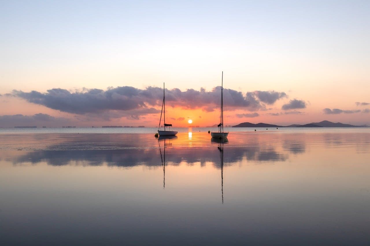 Barca solitaria sobre lago tranquilo con reflejo del amanecer, en el chat de Yupiltepeque