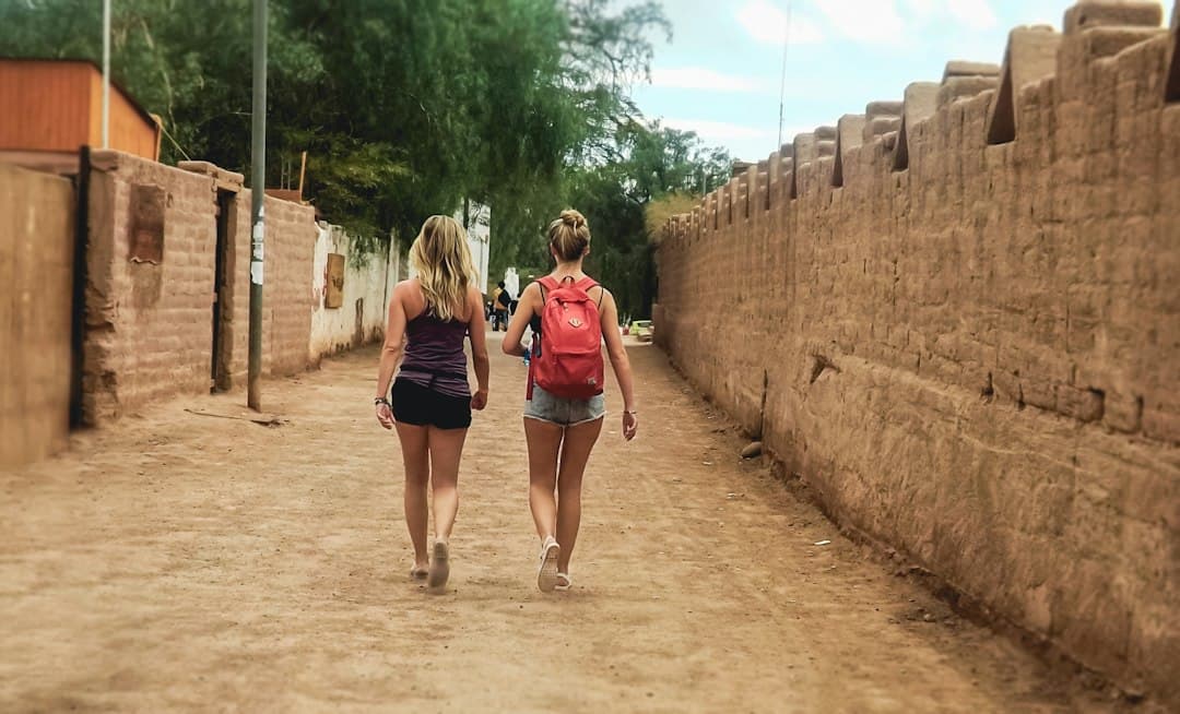 Dos mujeres caminando por un camino de tierra junto a un muro, en el chat de Quillón