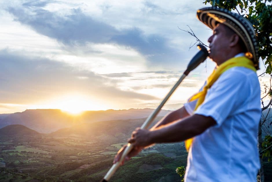 Hombre tocando un instrumento de pie en una colina al atardecer, en el chat de Guaranda