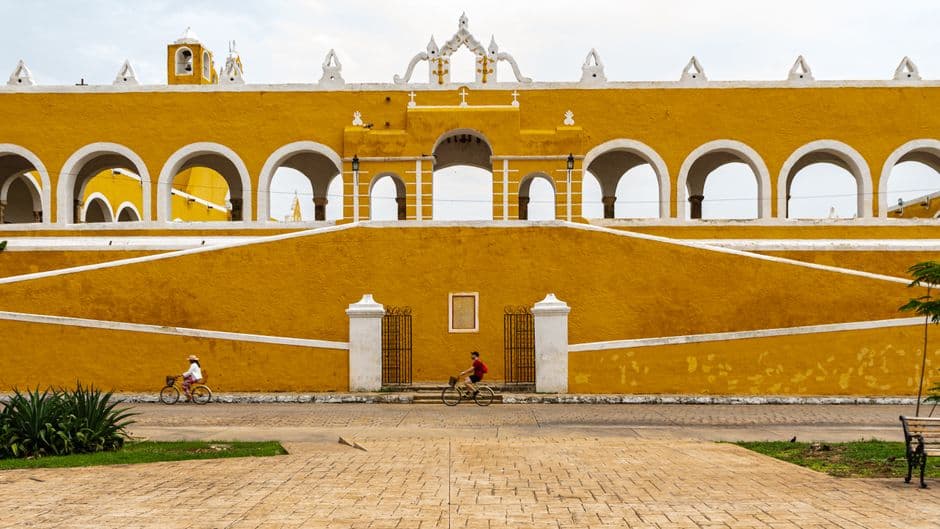 Un edificio colonial amarillo con ciclistas en Izamal, en el chat de Izamal