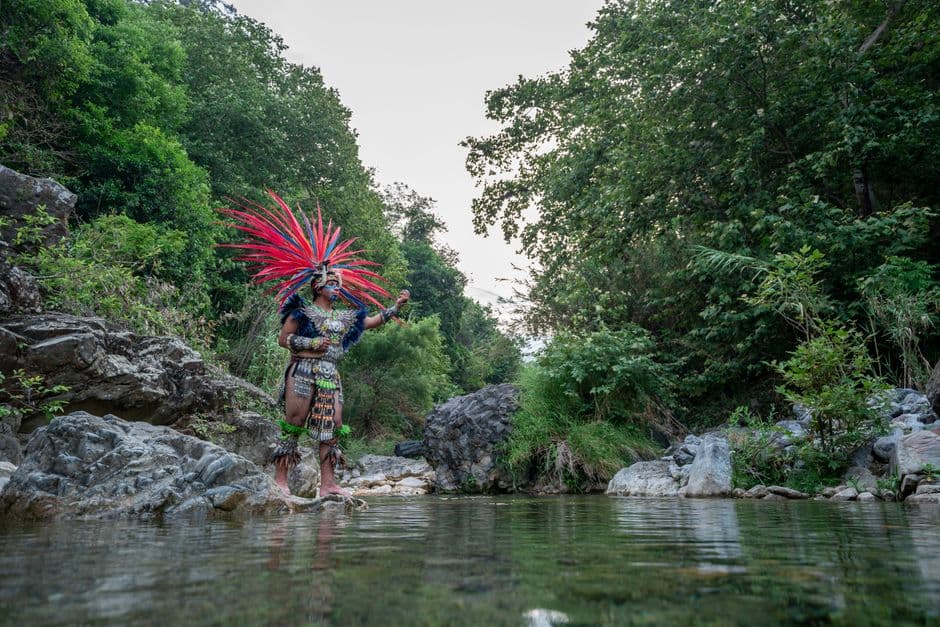Hombre con atuendo tradicional de pie junto a un lago, en el chat de Copala