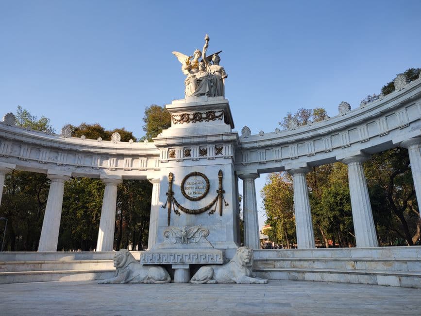 Monumento de piedra con columnas y escultura, rodeado de árboles, en el chat de Benito Juárez
