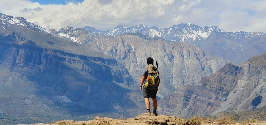 Hombre con mochila negra parado sobre roca marrón en montaña rocosa, en el chat de San José de Maipo