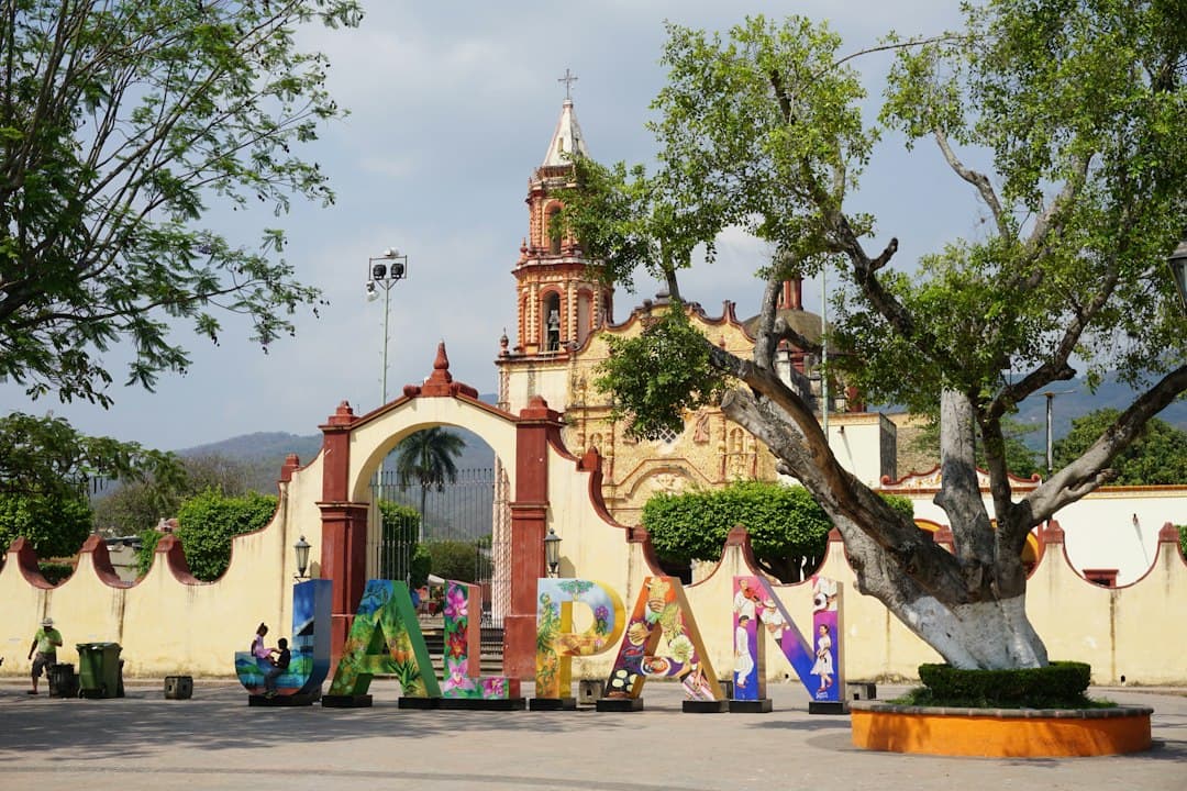Gente caminando por una calle con árboles y un edificio de hormigón, en el chat de Jalpan