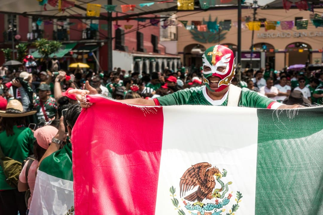 Persona enmascarada con la bandera de México en una multitud festiva, en el chat de Juan Galindo