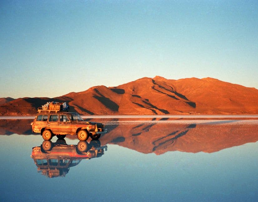 Jeep rojo detenido sobre arena, reflejado en agua tranquila, en la sala de chat de Sena
