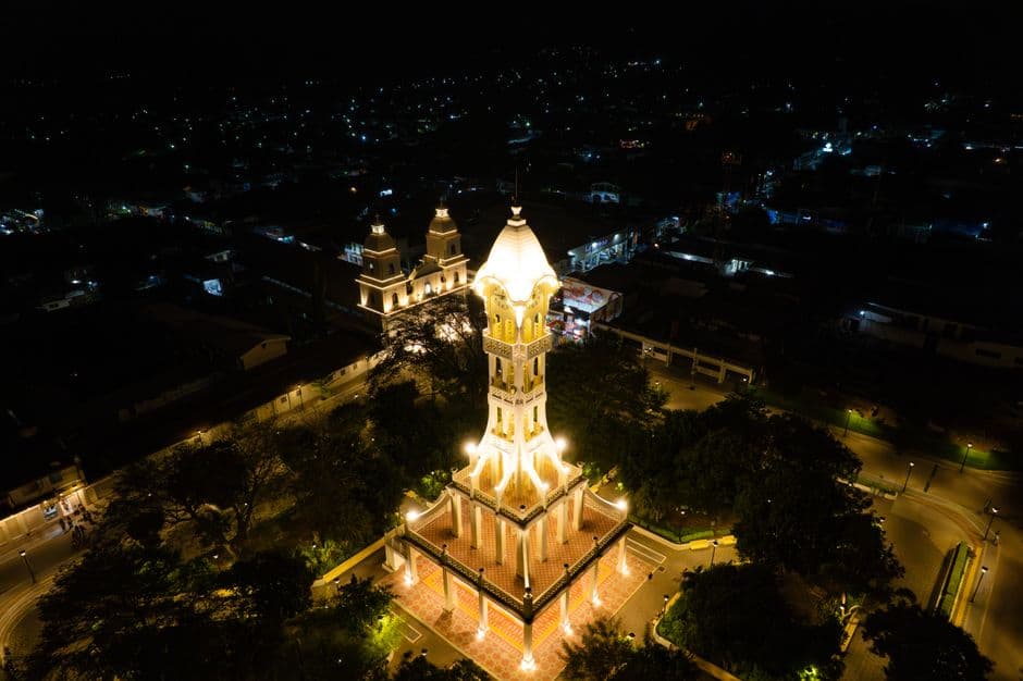 Torre campanario iluminada bajo cielo estrellado, rodeada de casas, en el chat de San Vicente