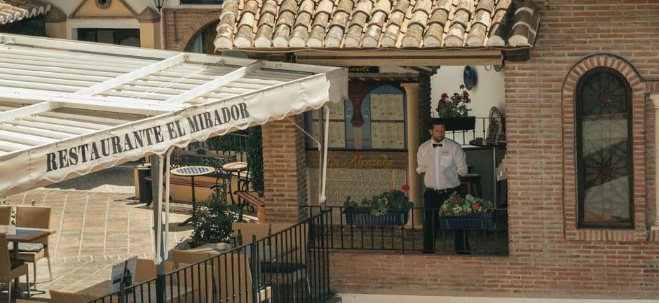 Un camarero junto a barandillas de un edificio de ladrillo, en la sala de chat de Alhaurín el Grande