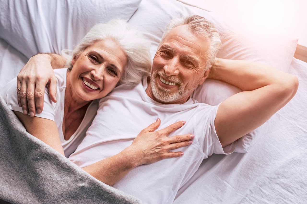 Pareja de jubilados sonrientes en la cama, en la sala de chat de Más de 60