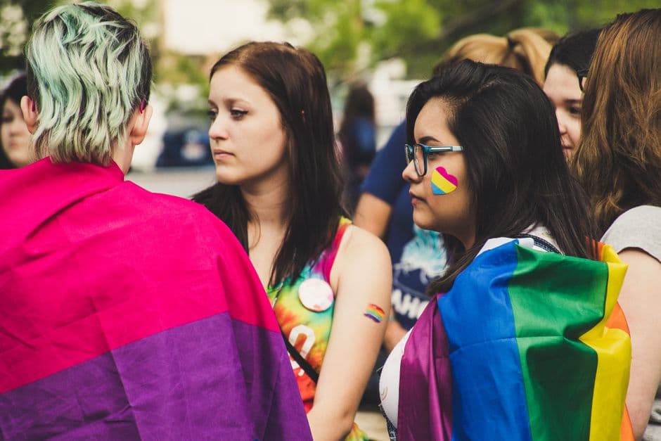 Personas celebrando juntas bajo una bandera arcoíris colorida, en la sala de chat de Chueca Sevilla