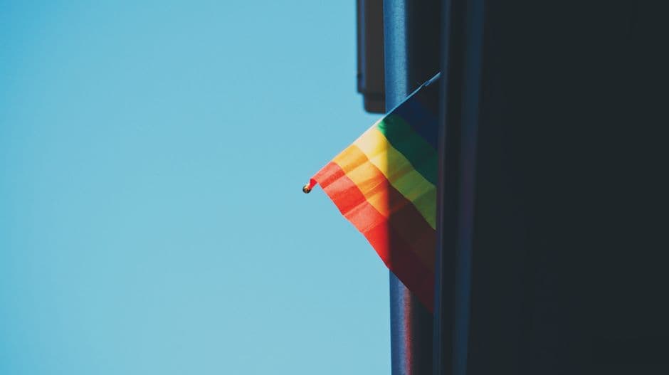 Bandera arcoíris colorida en ventana de edificio bajo cielo azul, en el chat de Chueca Málaga