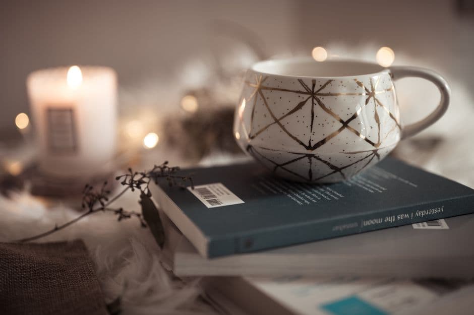 Taza de cerámica sobre libros apilados, luz tenue, en la sala de chat de Relatos Eróticos
