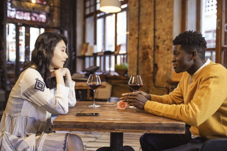 Pareja sonríe, se inclina sobre la mesa compartiendo café, en la sala de chat de Contactos