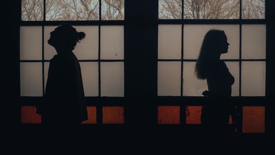 Pareja en silueta frente a gran ventana nocturna, tensionada, en la sala de chat de Cornudos
