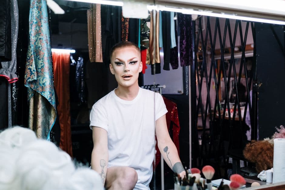 Drag queen se maquilla frente a espejo con luces, en la sala de chat de Travestis