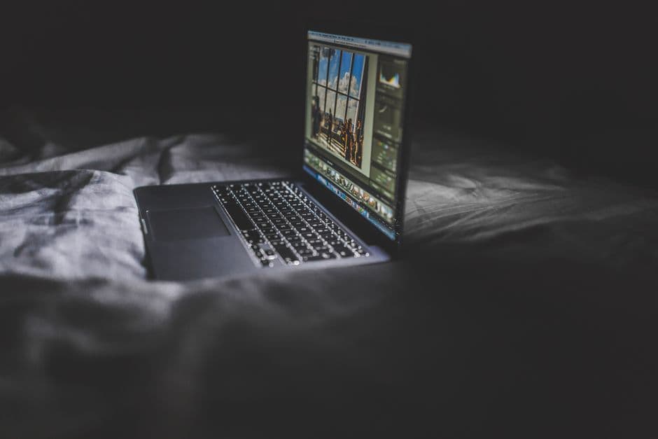 Joven con laptop en la cama bajo luz nocturna, en la sala de chat de Cibersexo