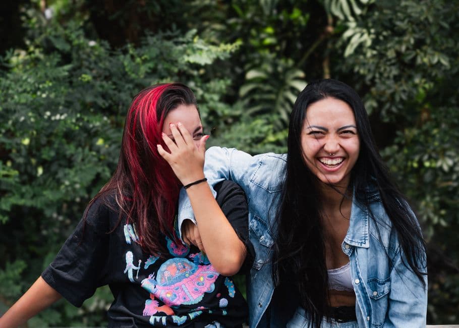 Tres amigas ríen mientras caminan bajo árboles verdes, en la sala de chat de Chatear
