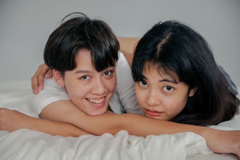 Pareja de mujeres sonrientes recostada en la cama, en el chat de Les Contactos